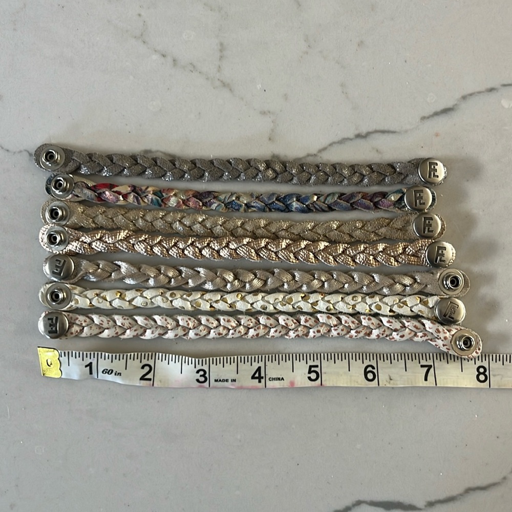 Bundle of seven small flourish leather braided bracelets in metallic colors.